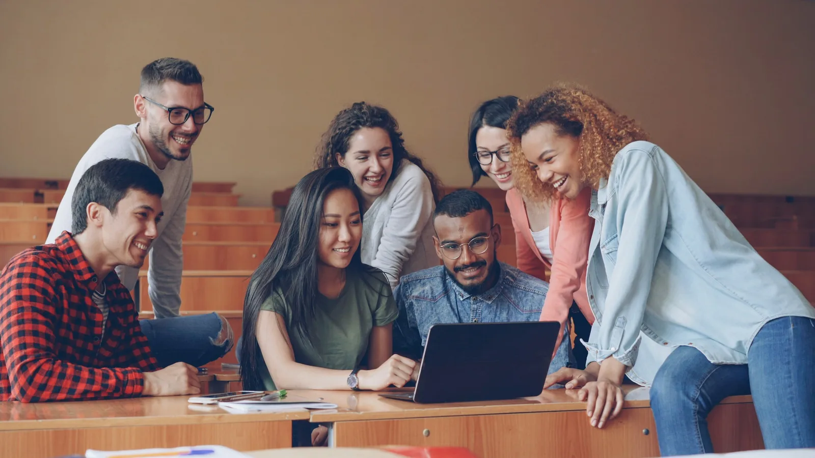 Young adults discussing work around a laptop in a classroom.