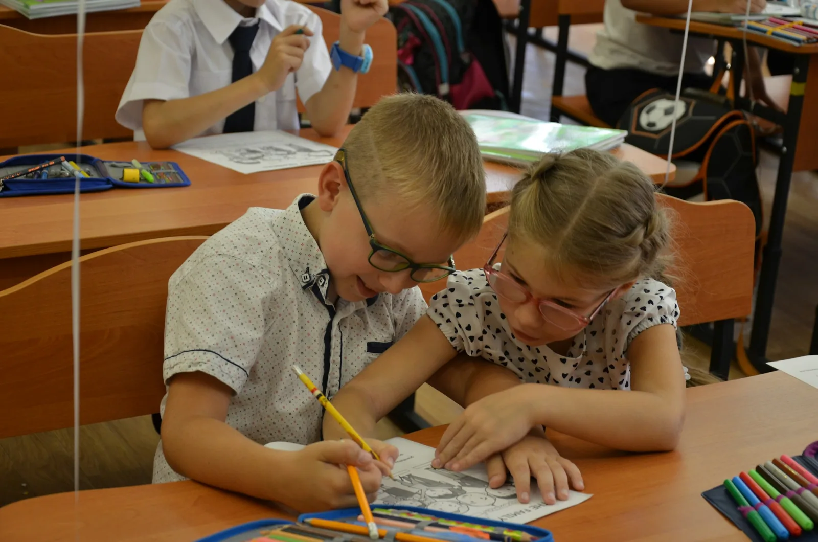 Two pupils drawing together at a classroom desk.