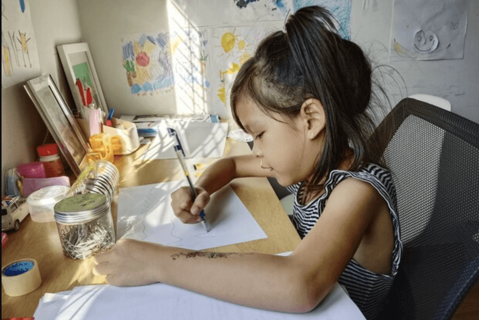 A child drawing at a desk with art materials.