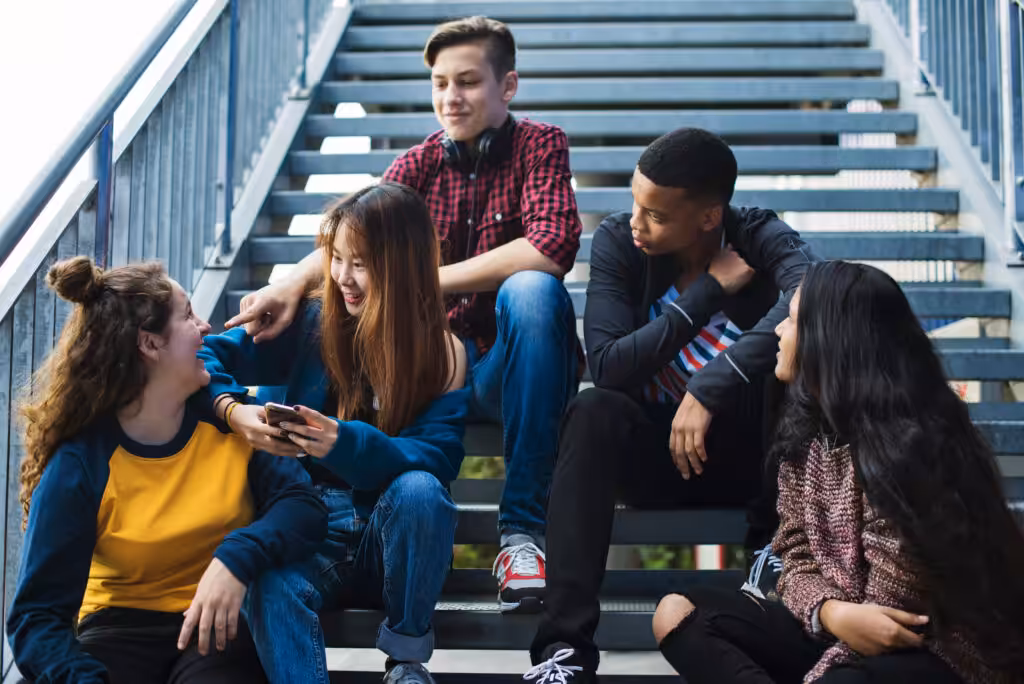 Diverse group of five teenagers sitting on school stairs, laughing and collaborating — representing international student teamwork in a design thinking school project