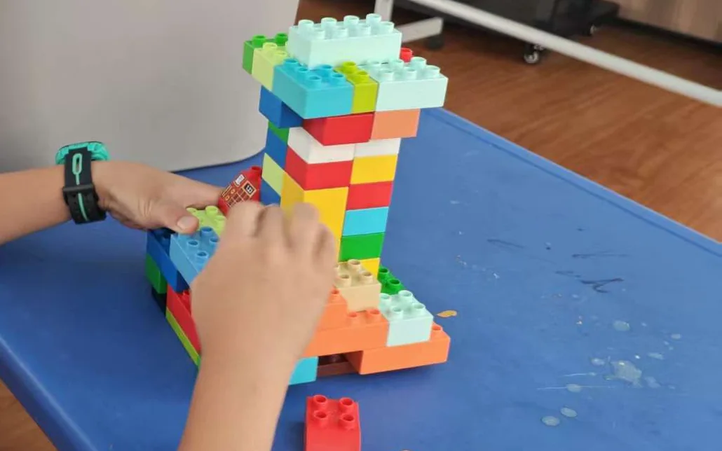 Un estudiante añade bloques a una torre de colores.