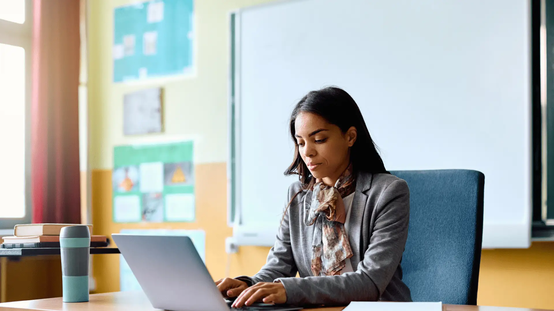Teacher using a laptop in a classroom, learning how to earn certificates on Class2Class.org