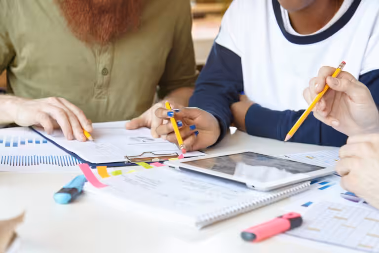 Two teachers reviewing a collaborative project checklist together at a table with papers and markers